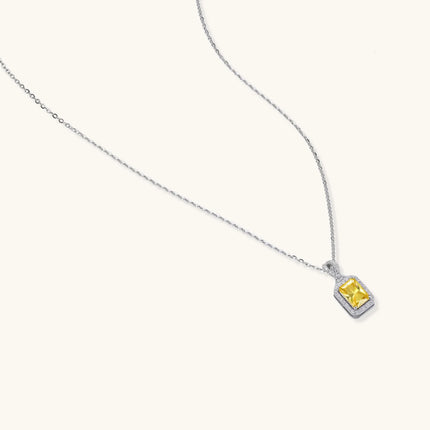 Rectangular yellow moissanite pendant in sterling silver halo setting on delicate chain against cream background.