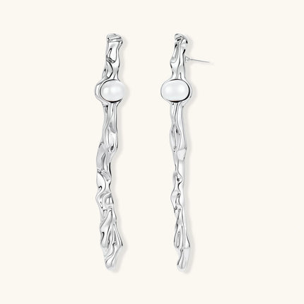 Sculptural silver drop earrings with flowing twisted design and white pearls on neutral background.