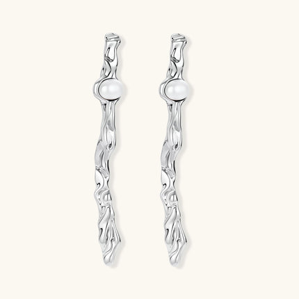 Sculptural silver drop earrings with flowing twisted design and white pearls on neutral background.