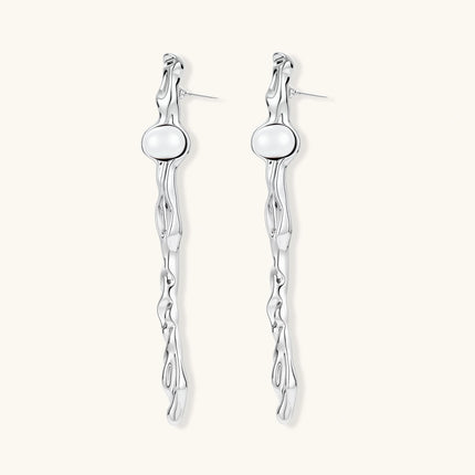 Sculptural silver drop earrings with flowing twisted design and white pearls on neutral background.