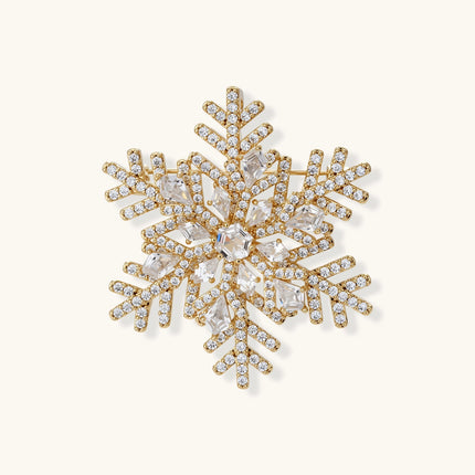 Ornate gold-plated snowflake brooch with geometric crystal pattern and sparkling zirconia stones on cream background.