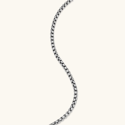 Silver stainless steel ankh pendant with skull motifs on vertical bar and textured ring top, on a box chain necklace.