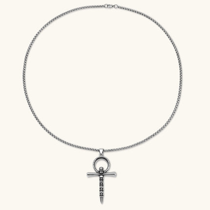 Silver stainless steel ankh pendant with skull motifs on vertical bar and textured ring top, on a box chain necklace.