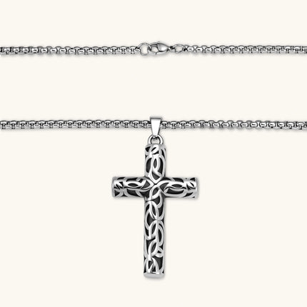 Silver stainless steel Celtic cross pendant with filigree vine pattern on a box chain, against a cream background.