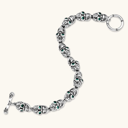 Silver stainless steel skull link bracelet with green crystal eye sockets and engraved detailing, toggle clasp closure.