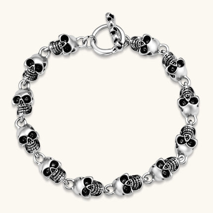 Silver stainless steel bracelet with linked 3D skull charms and a spring-ring clasp, oxidized black detailing, 225mm length.